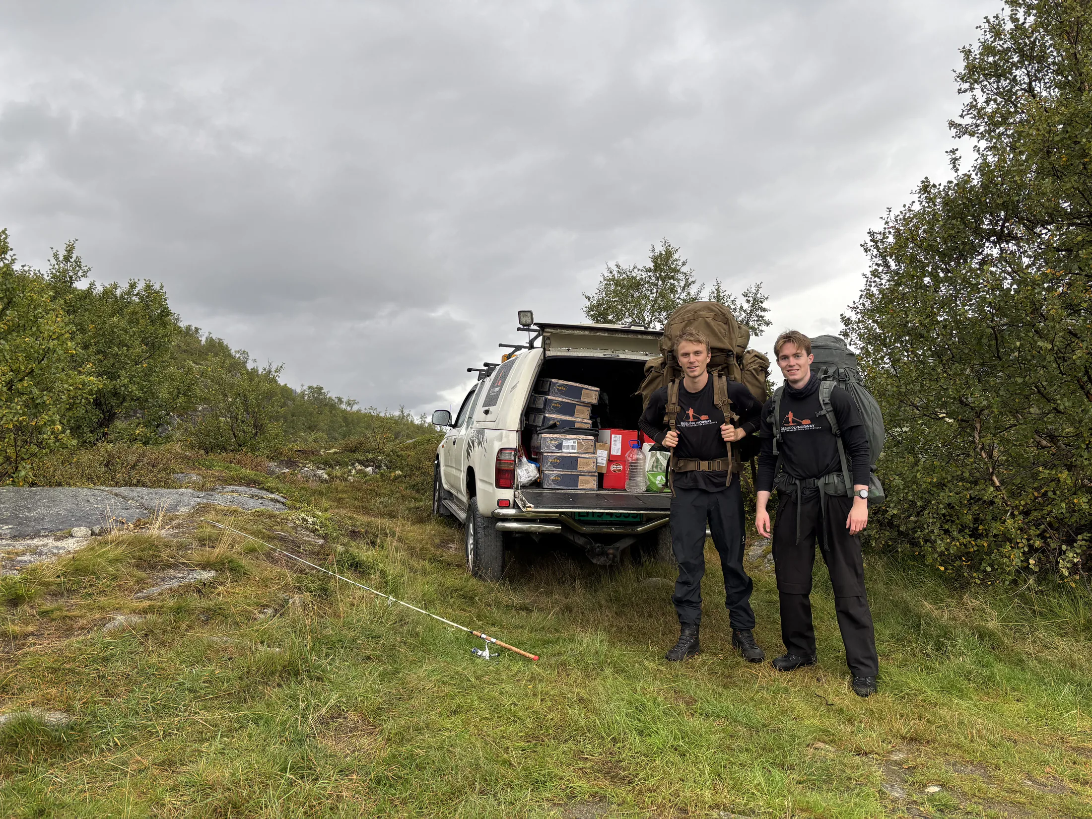 Two members of ResupplyNorway with large packs beside a car loaded with supplies